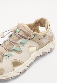 Beige mesh and synthetic shoe with turquoise accents, featuring a toggle lace system and a cushioned sole with a textured grip.