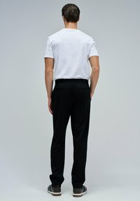 Pantalones negros con un corte relajado, que cuentan con una cinturilla elástica y dos bolsillos traseros, combinados con una camiseta blanca de manga corta y lisa.