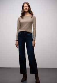 Beżowa bluzka z długim rękawem, zestawiona z ciemnoniebieskimi jeansami o prostych nogawkach. Jeansy mają przednie kieszenie i delikatny wzór przeszyć. Brązowe botki za kostkę.