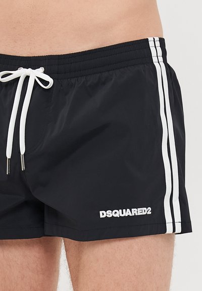Svarta badbyxor med vita sidostråk och vit dragsko, med DSQUARED2-logotyp på vänster lår.