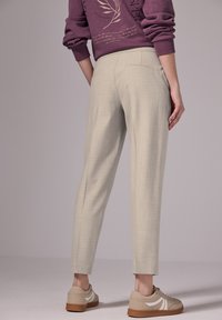 Lichtbeige, op maat gemaakte broek met een soepele textuur, slim fit en een subtiel ruitpatroon, gecombineerd met beige sneakers met witte accenten.