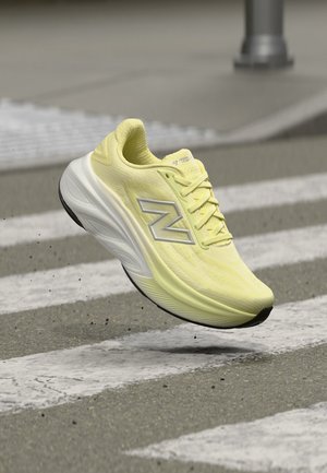 Geel-witte hardloopschoen met veters en logo, zwevend boven een zebrapad op asfalt.