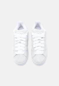 Fehér velúr sportcipő lapos, fehér fűzőkkel, kerek orral és törtfehér gumitalppal. Logó dombornyomott a nyelveken és az oldalán.