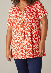 Blusa roja de manga corta con escote en V, con un patrón floral blanco. Tela suave y ligera con un corte holgado y detalle de plisado en la parte delantera.