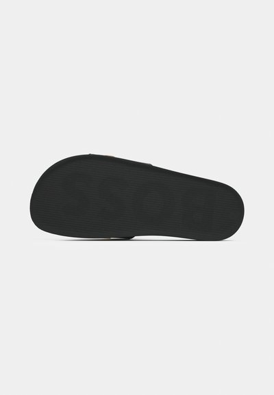 Semelle de chaussure en caoutchouc noir avec des rainures texturées et un bord arrondi. Présente un motif de logo en relief et une finition lisse.