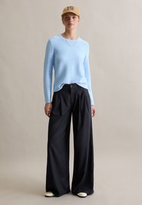 Lichtblauwe trui, zwarte wijde pijpen broek, beige pet met "15" borduring, witte schoenen, gestructureerde stof, losse pasvorm, eenvoudig ontwerp.