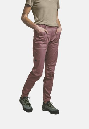 Persona che indossa pantaloni cargo malva con polsini elasticizzati, una t-shirt beige e scarpe da trekking grigie, in piedi con le mani nelle tasche.