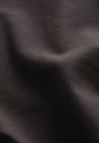 Prim-plan al unui material maro închis, neted, cu pliuri subtile și textură moale vizibilă sub o iluminare blândă.