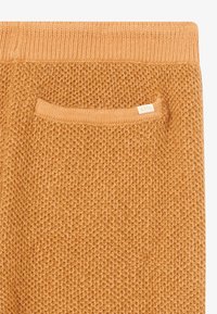 Strickpullover in warmem Orange, mit einem strukturierten Muster und einer kleinen Tasche mit einem Etikett an der Seite.