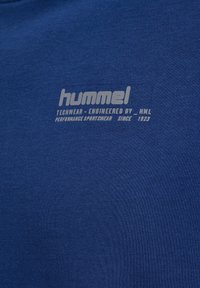 Blå bomull t-shirt med en grå Hummel-logotyp och text. Tyget har en mjuk textur och en klassisk rundad halsringning.