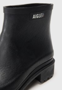 Bottine en caoutchouc noire avec une finition texturée, dotée d'une petite étiquette logo et d'une semelle épaisse à crampons. Forme lisse et arrondie.