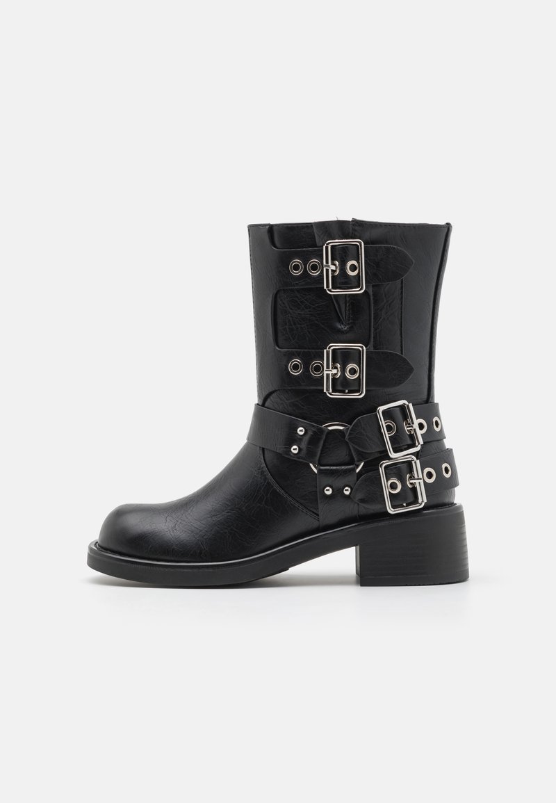 Bota de tornozelo preta em couro com quatro tiras de fivela prateadas, bico redondo e salto robusto. Apresenta material texturizado e detalhes laterais.
