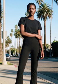 Noor naine mustas riietuses seisab päikesepaistelisel kõnniteel, taga on palmid ja tänaval pargitud autod.