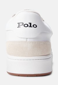 Bílé tenisky s hladkým koženým svrškem a béžovým semišovým akcentem na patě, s potiskem černého loga "Polo" a texturovanou gumovou podrážkou.