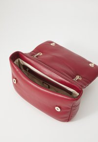 Borsa a mano rossa in pelle con una texture liscia, dotata di hardware dorato, tasca interna con zip e chiusura a busta con bottoni a pressione.