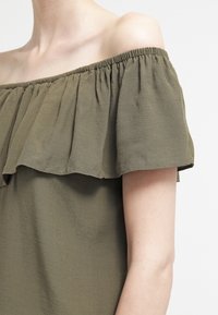 Olivengrøn off-shoulder top med en volang-krave, letvægtsstof og elastisk kant for en afslappet pasform.