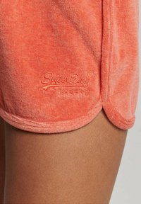 Shorts in spugna corallo con orlo arrotondato, logo ricamato "SuperDry" di colore abbinato, texture morbida e dettagli di design casual.