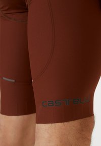 Maronenfarbene Radshorts aus dehnbarem Stoff, mit flachen Nähten und reflektierenden Akzenten. "Castelli"-Logo auf dem Bein gedruckt.