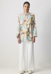 Long-sleeve button-up shirt with floral patterns in pastel colors, paired with wide white pants and sneakers. Smooth fabric texture.