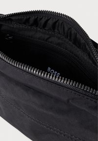 Fekete nejlon erszény cipzáros záródással, belső cipzáras zsebbel és sima tapintású anyaggal. A márkajelzés belül látható.