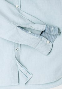 Camicia in lino azzurro chiaro con colletto button-down, bottoni bianchi e dettaglio a righe sul polsino. Tessuto morbido e design casual.