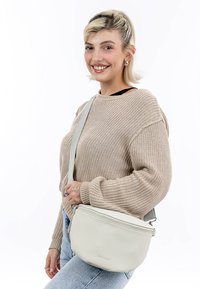 Hellgraue Leder-Crossbody-Tasche mit abgerundeter Form, Reißverschluss und verstellbarem Tragegurt, vor einem weißen Hintergrund gezeigt.