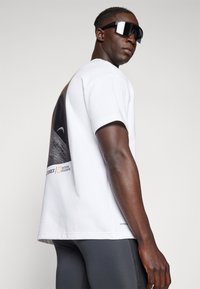 White short-sleeve t-shirt featuring a graphic print of a lunar landscape on the back, with branding in yellow and black accents.