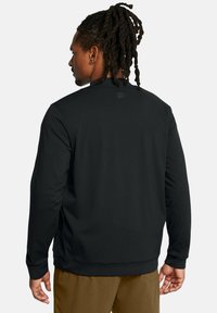 Schwarzer Pullover mit Rundhalsausschnitt, langen Ärmeln und seitlichen Schlitzen. Verfügt über ein markiertes Logo-Patch auf der Rückseite. Glatter, leicht dehnbarer Stoff.