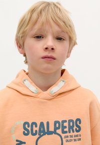 Ljusorange huvtröja med dragsnodd, med en blå grafisk tryck som läser "SCALPERS". Mjuk tygtextur, minimalistisk design.