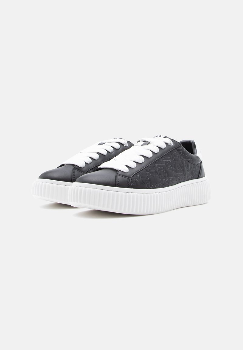 Zapatillas negras de cuero con cordones blancos, suela blanca estriada y detalles texturizados en los laterales. Diseño simple con acentos mínimos.