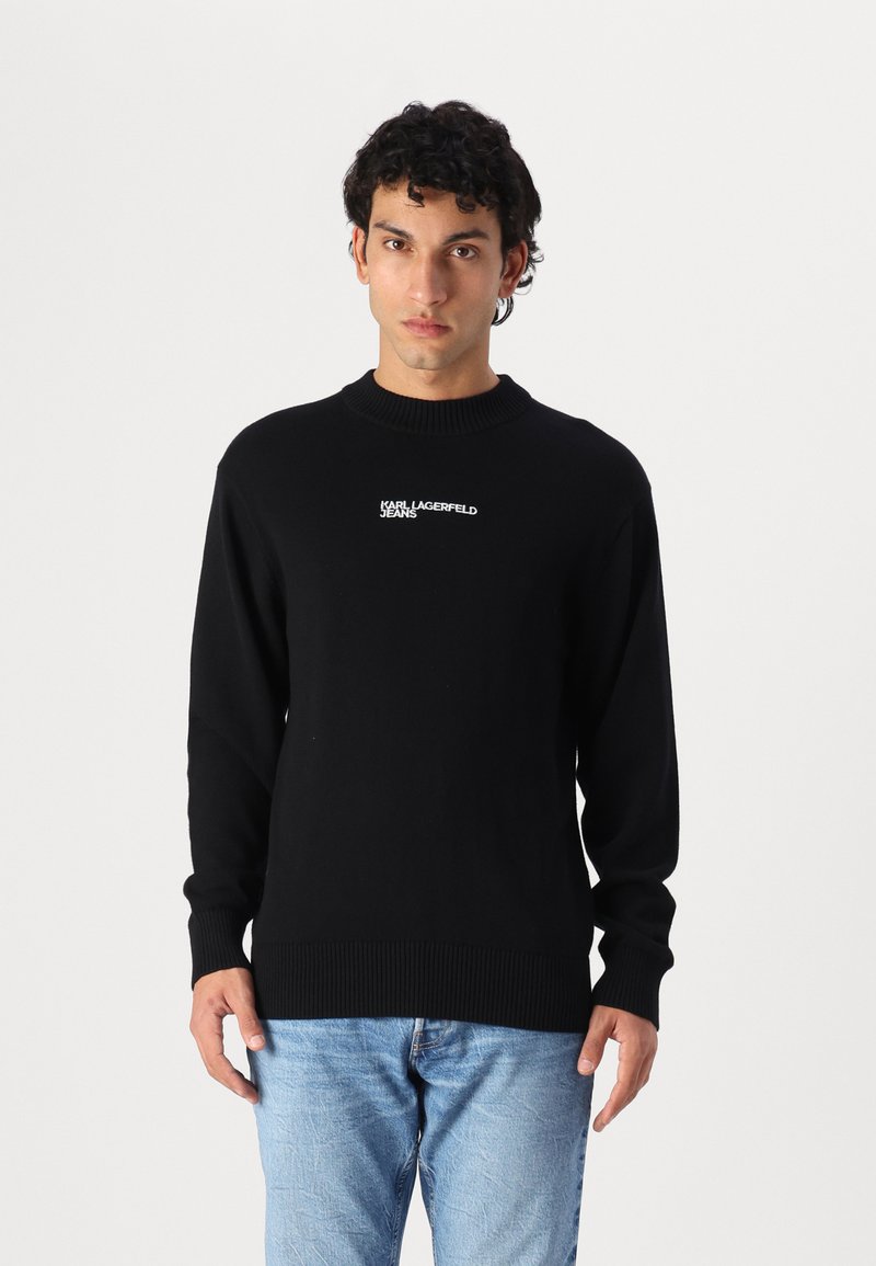 Juodas megztinis su kepurėmis, su gipiūro rankovėmis ir apatine dalimi, su balta "Karl Lagerfeld Jeans" logotipu ant krūtinės. Lygi tekstūra, apvali iškirptė.