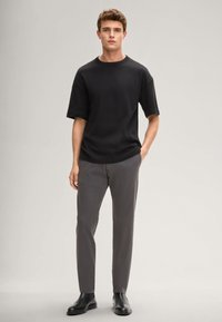 Czarny t-shirt z krótkim rękawem i okrągłym dekoltem, zestawiony z szarymi spodniami o dopasowanym kroju i czarnymi skórzanymi butami. Prosty design, gładka faktura.