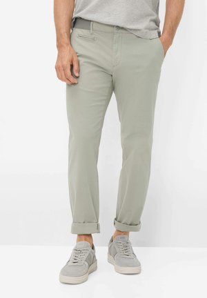 Mann trägt hellgraue Freizeithosen, an den Bündchen hochgekrempelt, mit passenden grauen Sneakers und einem in die Hose gesteckten grauen T-Shirt.