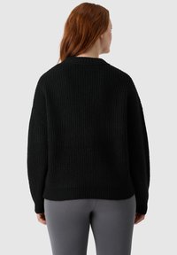 Czarny sweter dzianinowy o luźnym kroju, z prążkowaną fakturą, szerokimi rękawami i subtelnym krojem z opadającym ramieniem. Połączony z szarymi legginsami.