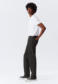 Jeans de ganga preta com um corte descontraído, apresentando um design clássico de cinco bolsos. Combinados com uma t-shirt branca simples e ténis pretos.