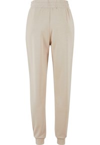 Beige joggebukser laget av myk stoff. Elastisk midje, to sidelommer, innsnevring ved bena og ribbede mansjetter ved anklene.