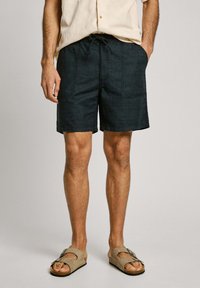 Bañador azul oscuro en tejido ligero con cintura de cordón, que cuenta con dos bolsillos laterales y un diseño limpio y simple.