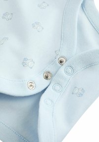 Une grenouillère en coton bleu clair avec un petit motif d'ours, présentant des fermetures à pression en bas et des bords de cou et de manches en jersey doux.