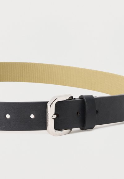 Μαύρη δερμάτινη ζώνη με ασημένια ορθογώνια αγκράφα και μπεζ εσωτερική επένδυση, τοποθετημένη επίπεδη πάνω σε λευκή επιφάνεια.