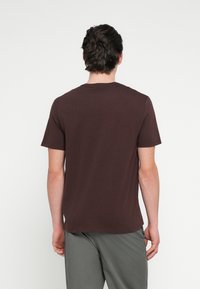 Smeđa majica kratkih rukava od pamuka, s okruglim izrezom i opuštenim krojem, u kombinaciji sa sivim hlačama.