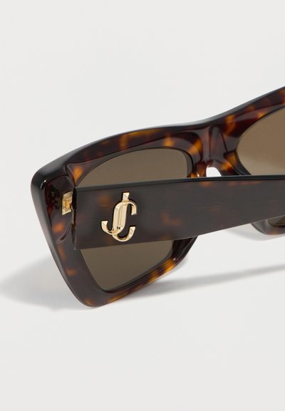 Γυαλιά ηλίου με μοτίβο χελώνιας και σκούρους φακούς, που διαθέτουν χρυσό λογότυπο "JC" σε διαπλεκόμενο σχέδιο στο μπράτσο του πλαισίου.