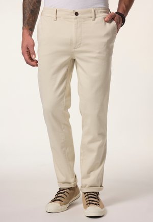 Beige chinos with a slim fit, made of cotton blend fabric. Features a button closure and rolled cuffs. Worn with light brown sneakers.