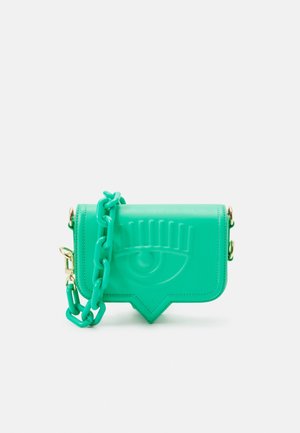 Borsa a tracolla verde con motivo di occhio in rilievo e tracolla a catena spessa su sfondo bianco.