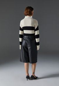 Knitted turtleneck sweater in cream with black horizontal stripes, paired with black leather shorts. Sleek black high-heeled shoes complete the look.