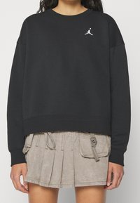 Felpa nera con maniche lunghe, colletto girocollo e design corto. Presenta un logo Jumpman bianco sul petto. Tessuto morbido.