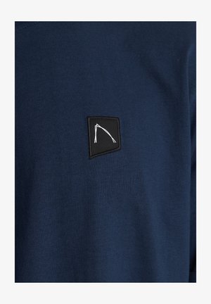 Námornícky modré tričko s krátkym rukávom vyrobené z bavlny, s malou čiernou vyšívanou nášivkou s bielym geometrickým vzorom.