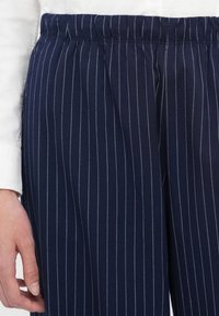 Marineblauwe streeppantalon met een elastische tailleband. De stof heeft een zachte textuur en beschikt over dunne witte verticale strepen.