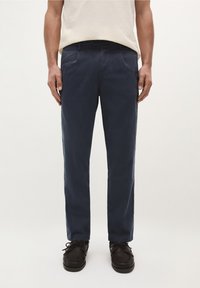 Chinos blu navy in cotone, con vestibilità dritta, tasche laterali e una texture liscia, abbinati a scarpe stringate scure.
