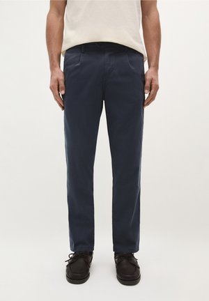Chinos azul marino de algodón, con un corte recto, bolsillos laterales y una textura suave, combinados con zapatos de cordones oscuros.