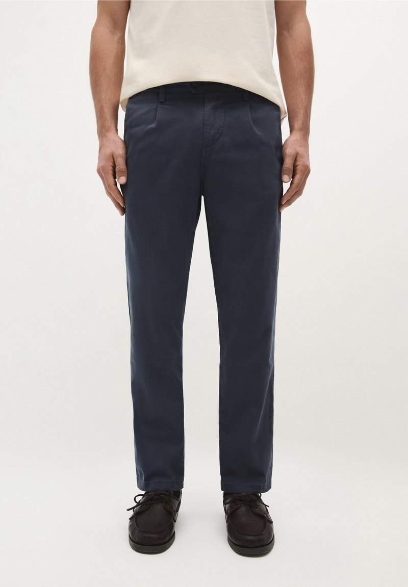 Chinos blu navy in cotone, con vestibilità dritta, tasche laterali e una texture liscia, abbinati a scarpe stringate scure.